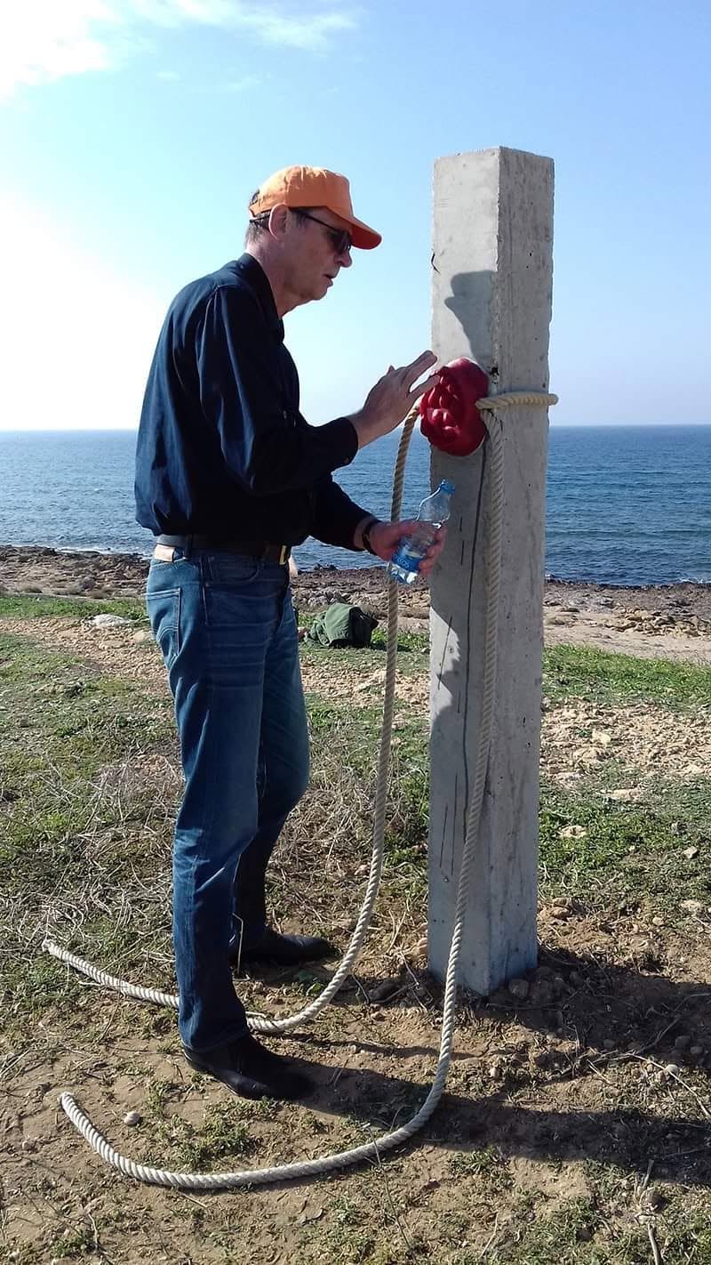 A man installs a rope and a red element on a concrete post by the sea